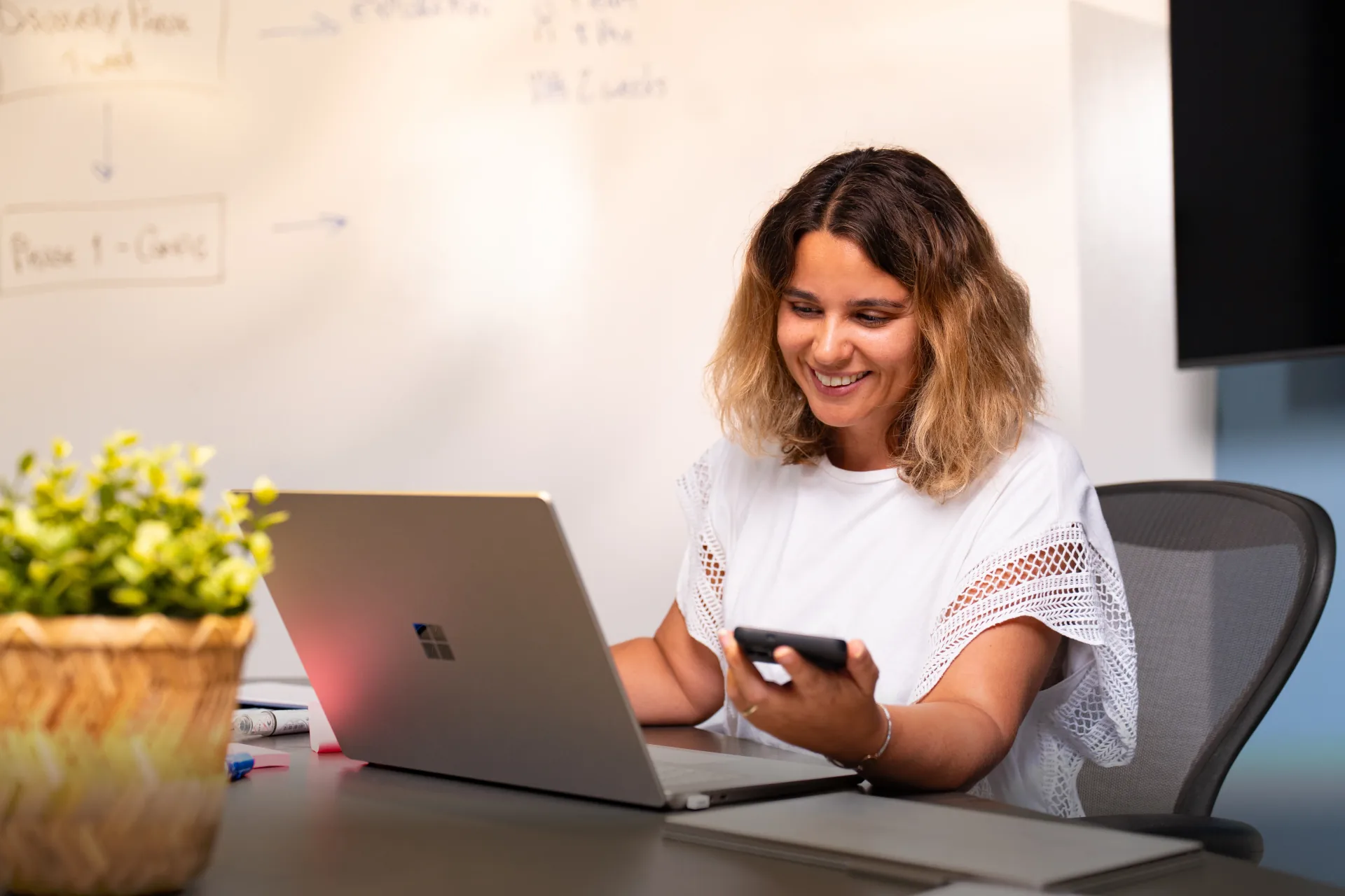 Professional woman at office desk smiling while working with personalized AI assistant